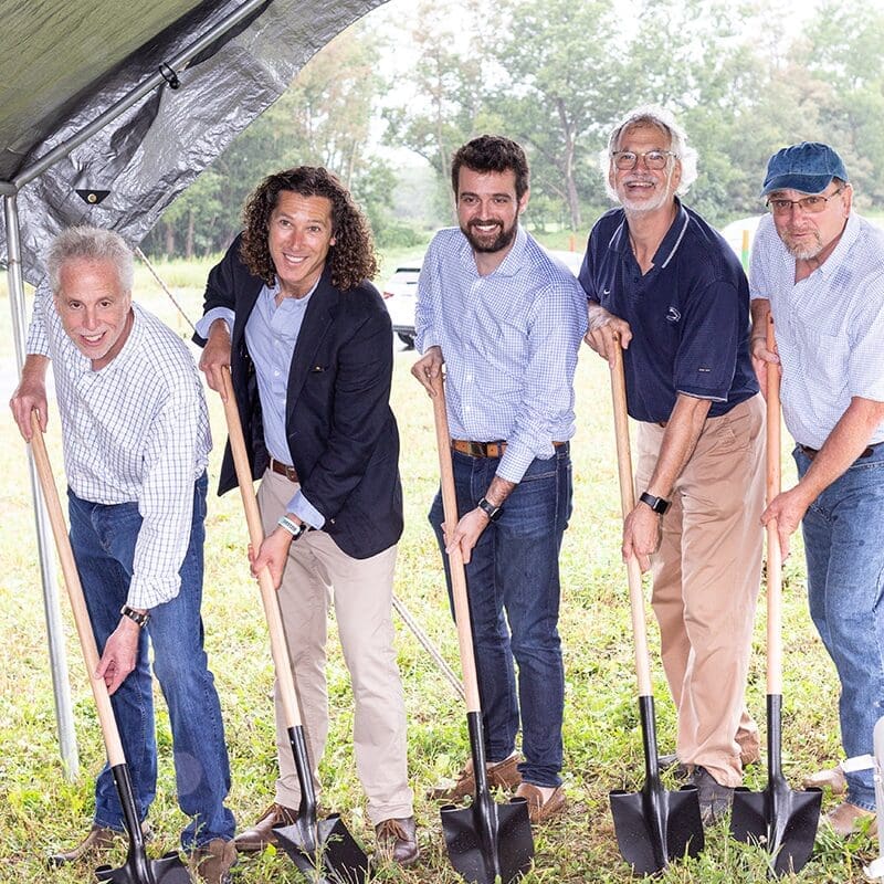 Executive team at a luxury home builder's groundbreaking event, holding shovels for the ceremonial first dig.